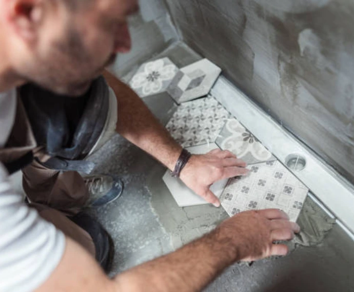 Contractor carefully laying decorative hexagonal patterned floor tiles with adhesive during a bathroom reconstruction or post-water damage restoration rebuild