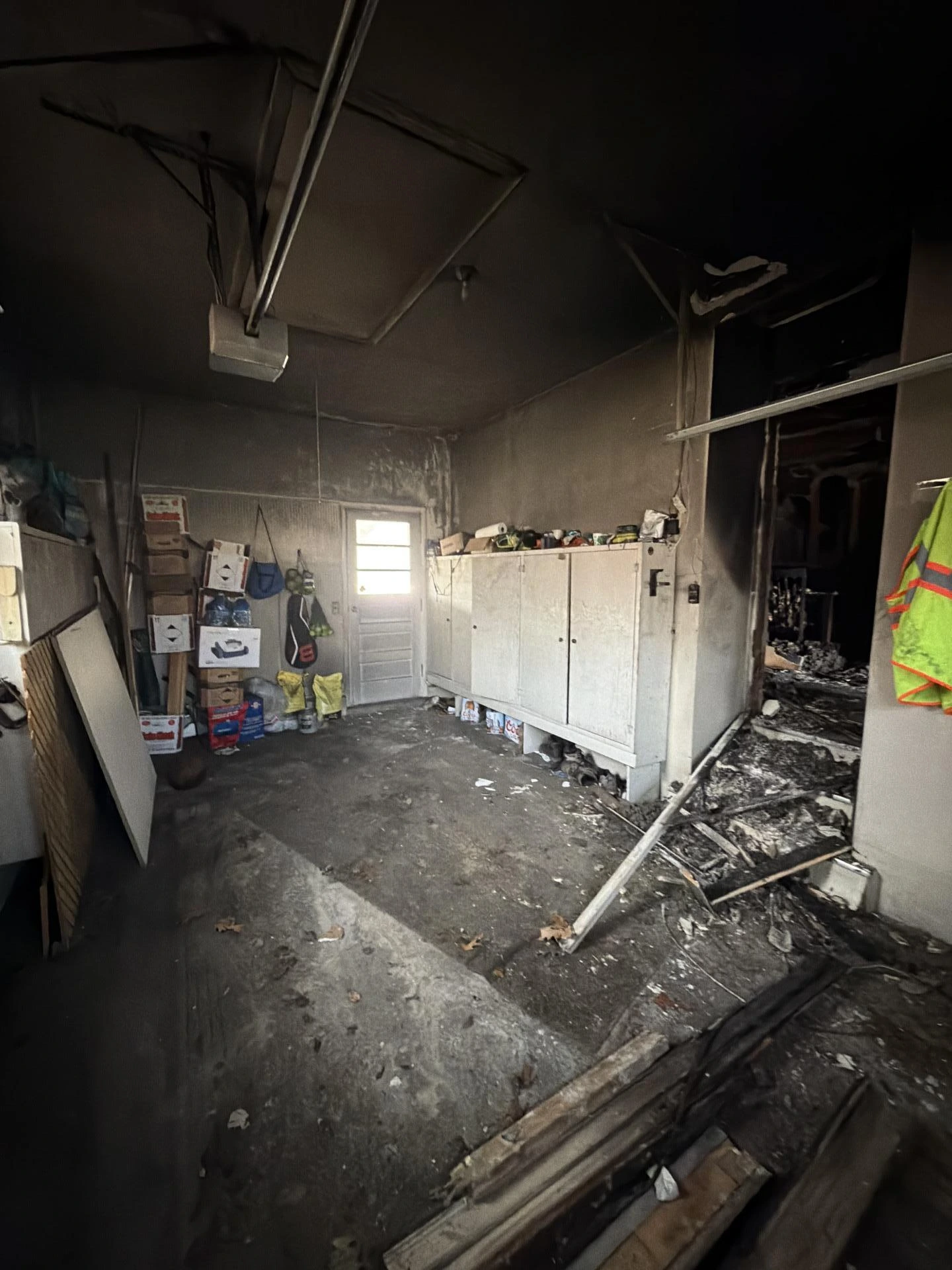 Fire-damaged garage interior with soot-blackened ceiling, charred debris on the floor, smoke-stained storage cabinets, and scattered burned belongings requiring fire damage restoration