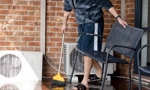 homeowner sweeping water from patio after flooding near outdoor AC unit