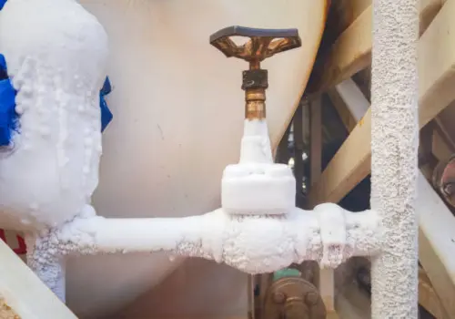 Heavily frost-covered shut-off valve and frozen pipes in a utility space, showing severe freeze damage risk requiring emergency plumbing and water damage restoration