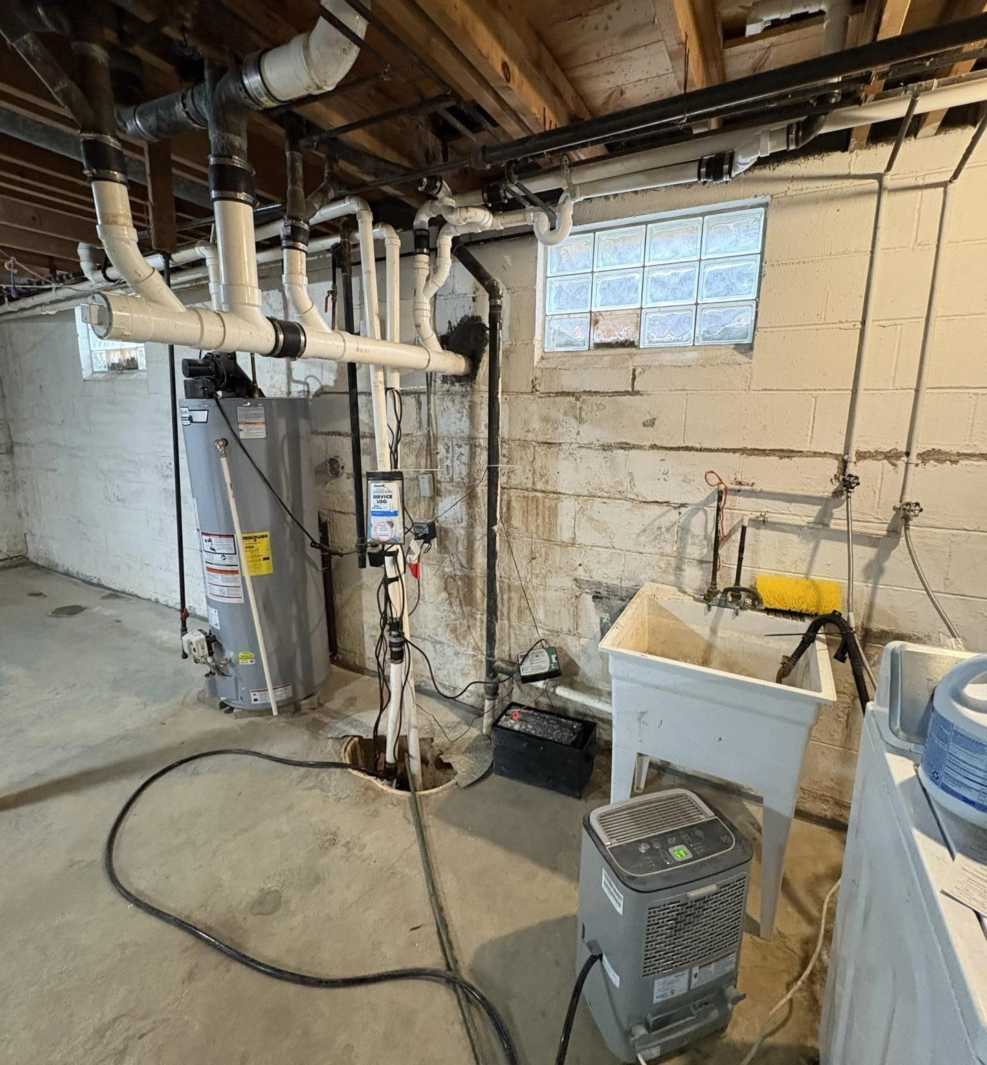 basement sump pump pit with discharge piping, water heater, utility sink, and dehumidifier managing moisture in a damp foundation area