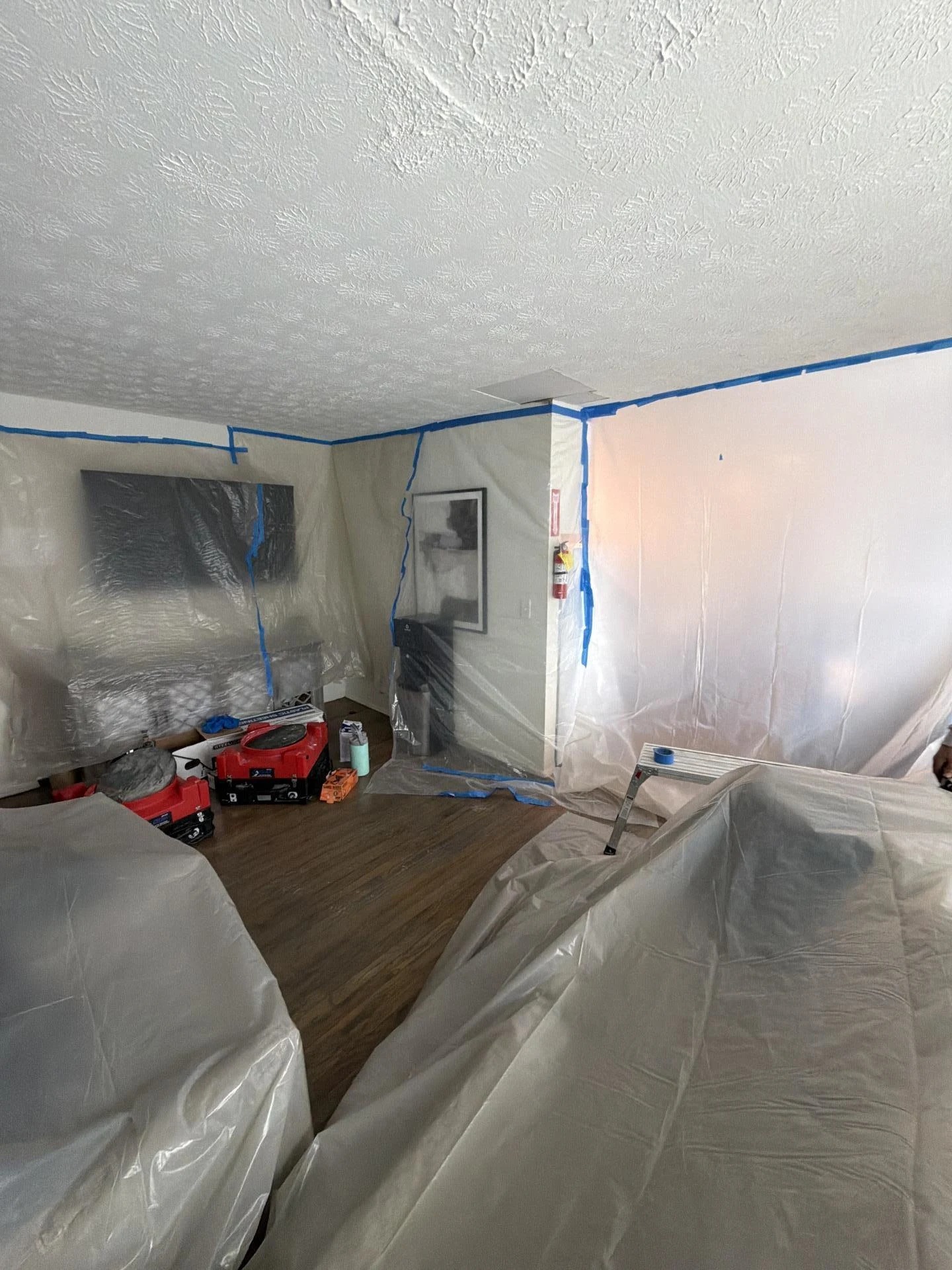 water damage containment setup with plastic barriers, covered furniture, and drying equipment in living room
