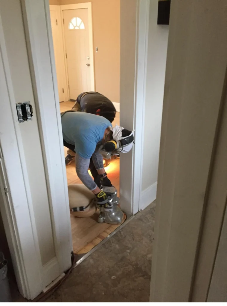 Restoration technician wearing a respirator mask using a floor drying or extraction tool at a doorway threshold during water damage remediation and flooring dryout services