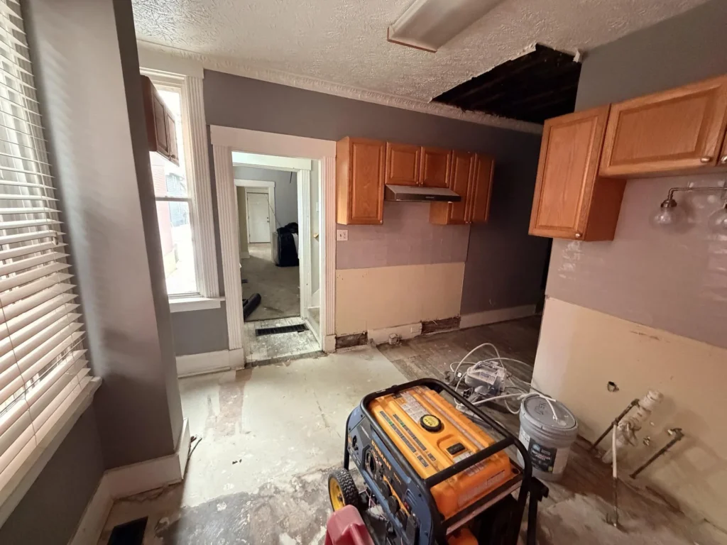 Bedroom staging area with two removed toilets on black plastic, large cardboard moving boxes, wall mirror leaning, decorative wall pieces, ceiling fan, carpeted floor during restoration
