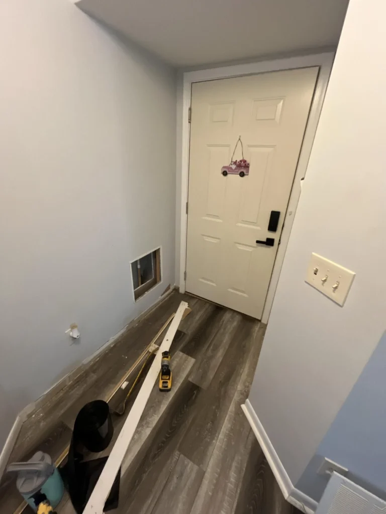 Entryway with new gray luxury vinyl plank flooring installed, front door with decorative ornament, baseboard removed from lower wall section