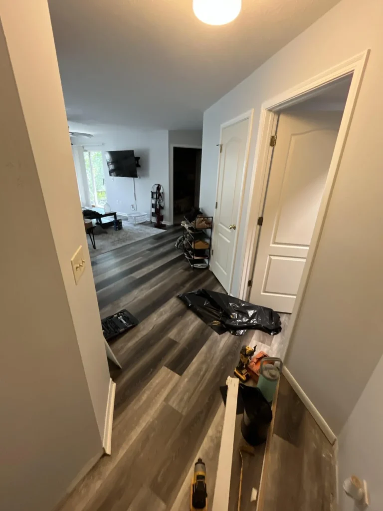 Hallway with newly installed gray luxury vinyl plank flooring looking toward living room, remediation tools and trash bags on floor during restoration