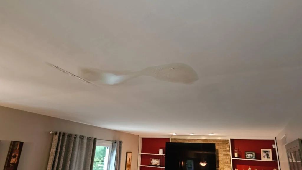 Wide-angle view of living room ceiling showing large water-damaged bulging area above seating area, red accent wall with built-in shelves and fireplace visible below