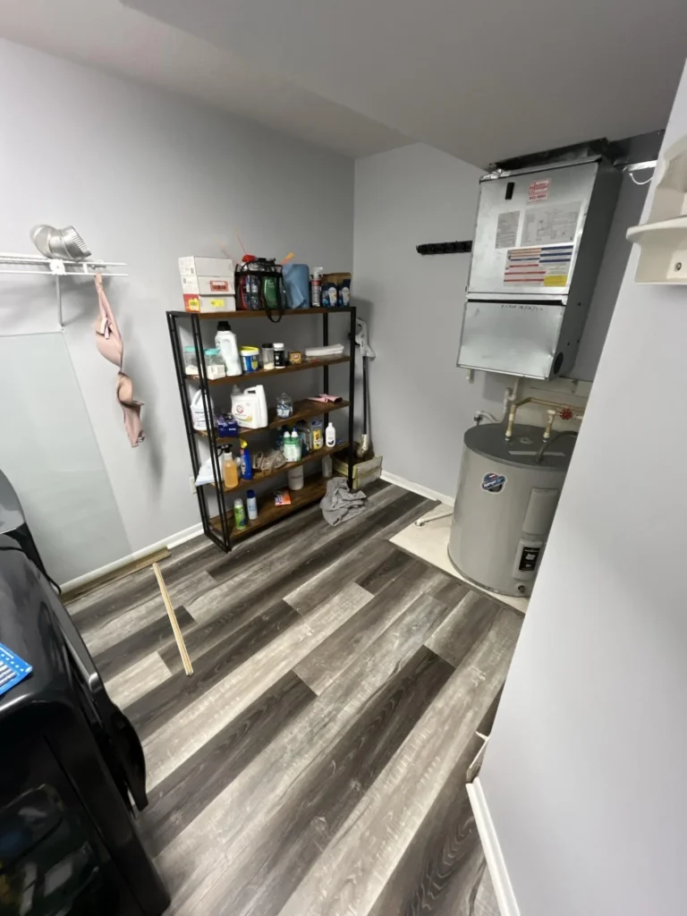 Completed utility and laundry room with new gray luxury vinyl plank flooring, supply shelving, water heater, and furnace after water damage restoration
