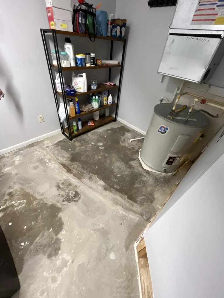 Utility room with bare concrete subfloor after flooring removal showing water heater, furnace unit, and electrical panel following water damage