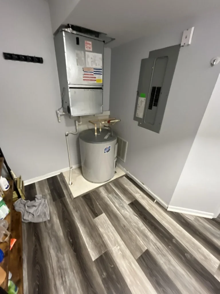 Utility room with new gray luxury vinyl plank flooring installed around water heater and furnace, electrical panel visible on wall